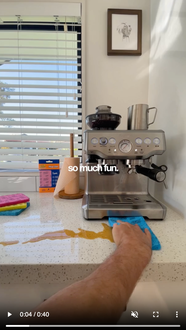 Nathan using a blue Mop Ups cloth to wipe a coffee spill beside his coffee machine